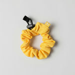Yellow scrunchie with a black clip on a light gray background