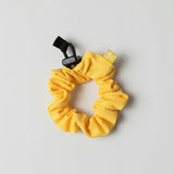 Yellow scrunchie with a black clip on a light gray background
